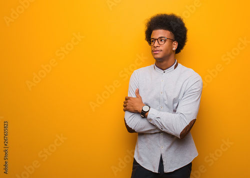 Young african american man over an orange wall smiling confident and crossing arms, looking up