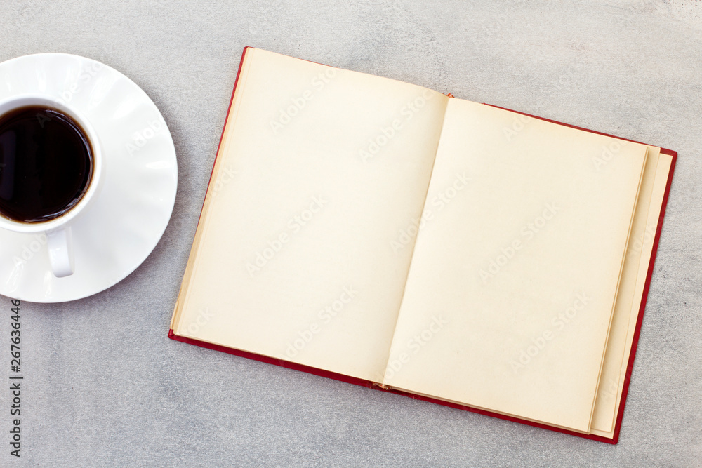 Open notebook with cup of coffee on gray background. Open notebook with cup of coffee on gray background.