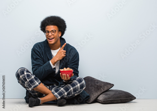 Young black man sitting and having a breakfast pointing to the side with finger © Asier