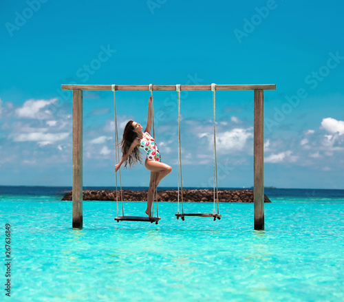 Beautiful woman swinging in the Indian Ocean over tropical landscape, Maldives island background.