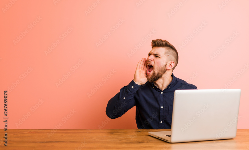 Young man working with his laptop shouting and holding palm near opened mouth. Young man working with his laptop shouting and holding palm near opened mouth.