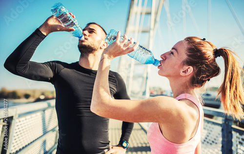 Rest after exercising. Thirsty sportsman and sportswoman drinking water after training outdoors. Fitness, sport, lifestyle concept