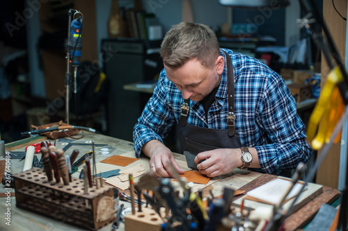 Man working with leather textile at a workshop. Concept of handmade craft production of leather goods.