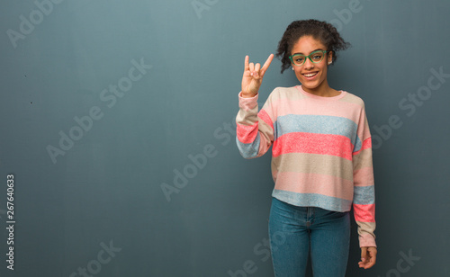 Foto Young african american girl with blue eyes doing a rock gesture
