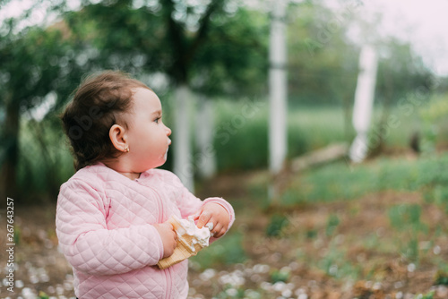 little girl in the garden on the background of greenery and trees very cute eating ice cream finger in a waffle Cup
