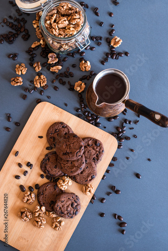 Freshly made coffee in old rustic Turkish coffee pot on dark background with coffee beans, chocolate cookies, sugar and walnuts – view with copy space. Aroma beverage drink. Flat lay