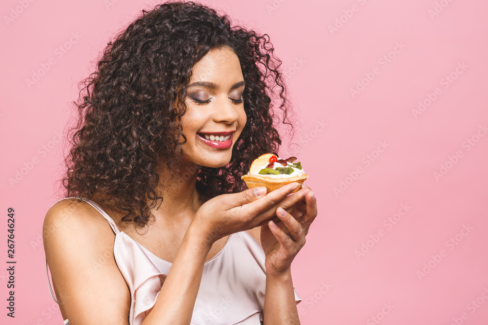 Black american african happy woman with curly afro hair style making a mess eating a huge fancy dessert over pink background. Eating cupcake. Black american african happy woman with curly afro hair style making a mess eating a huge fancy dessert over pink background. Eating cupcake.