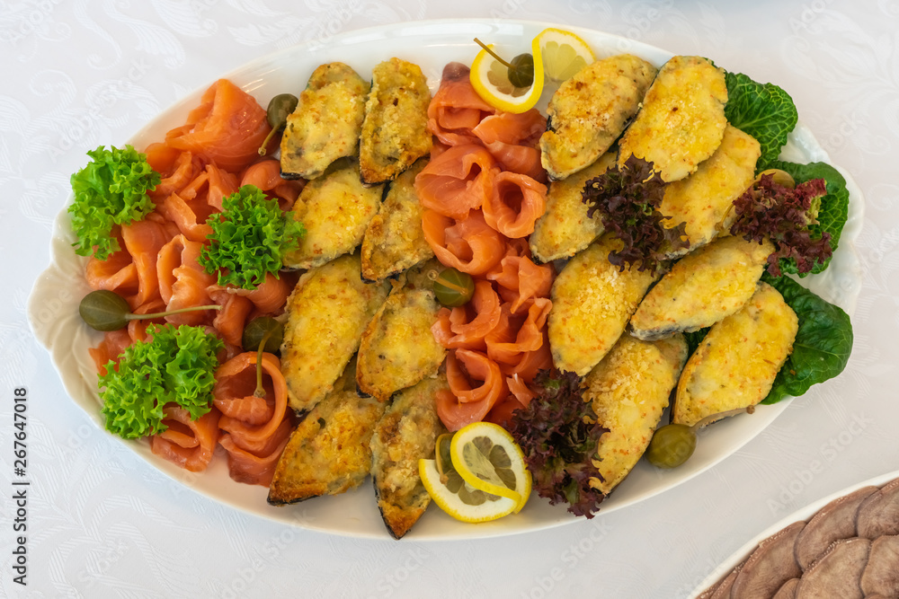 Tasty breaded fish fillet with salted red fish slices, green salad and lemon on white plate. Luxury dinner on banquette. Delicious restaurant menu. Tasty breaded fish fillet with salted red fish slices, green salad and lemon on white plate. Luxury dinner on banquette. Delicious restaurant menu.