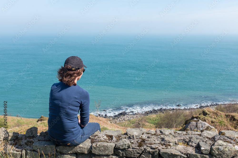 Woman looking at ocean back to camera, sunny day