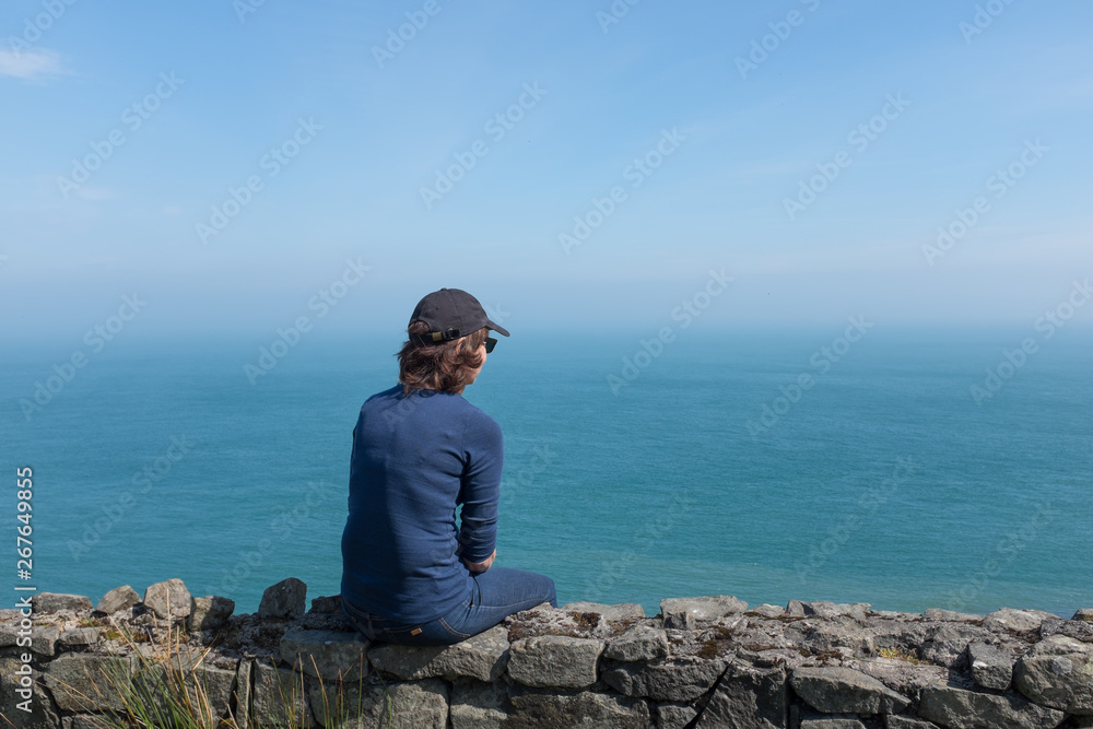 Woman looking at ocean back to camera, sunny day