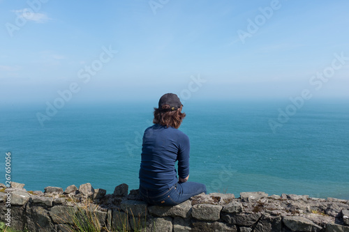 Woman looking at ocean back to camera, sunny day