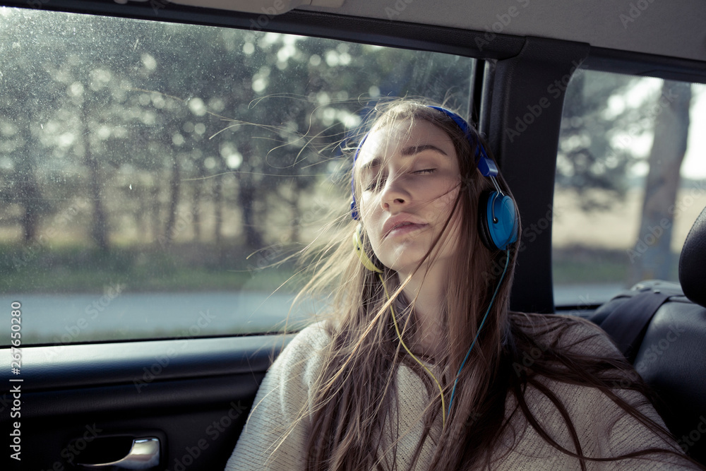 Young woman with windswept hair in a car wearing headphones Young woman with windswept hair in a car wearing headphones