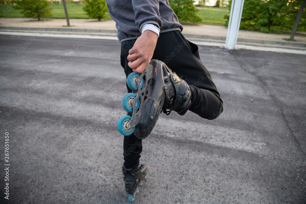 Crop back view of young cool man in sportswear holding roller skate with hand on road in park Crop back view of young cool man in sportswear holding roller skate with hand on road in park