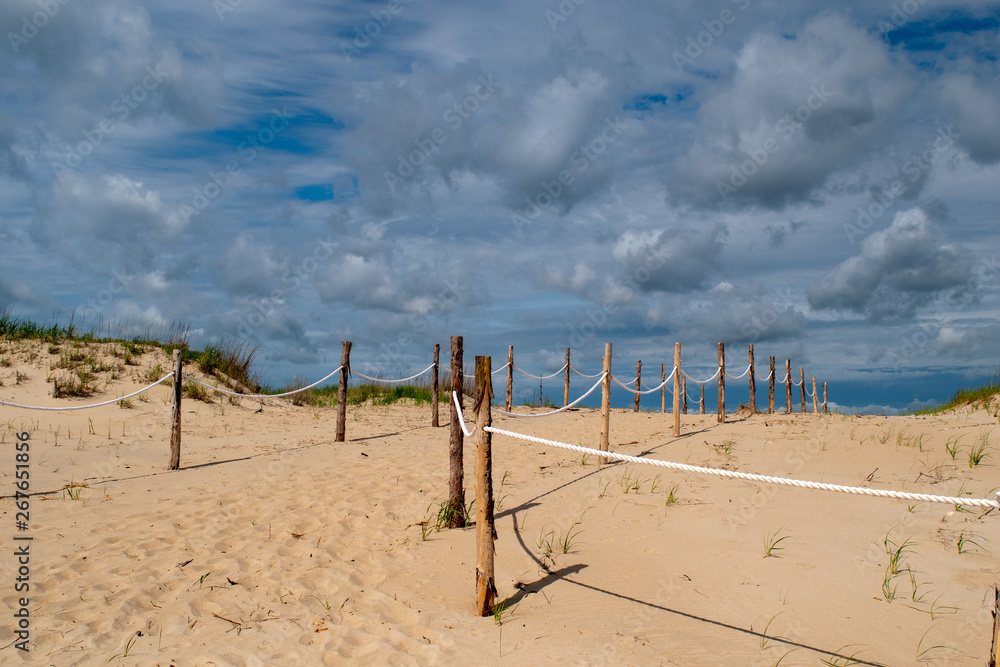 Entrance to the beach through the dunes and under cloudy blue skies