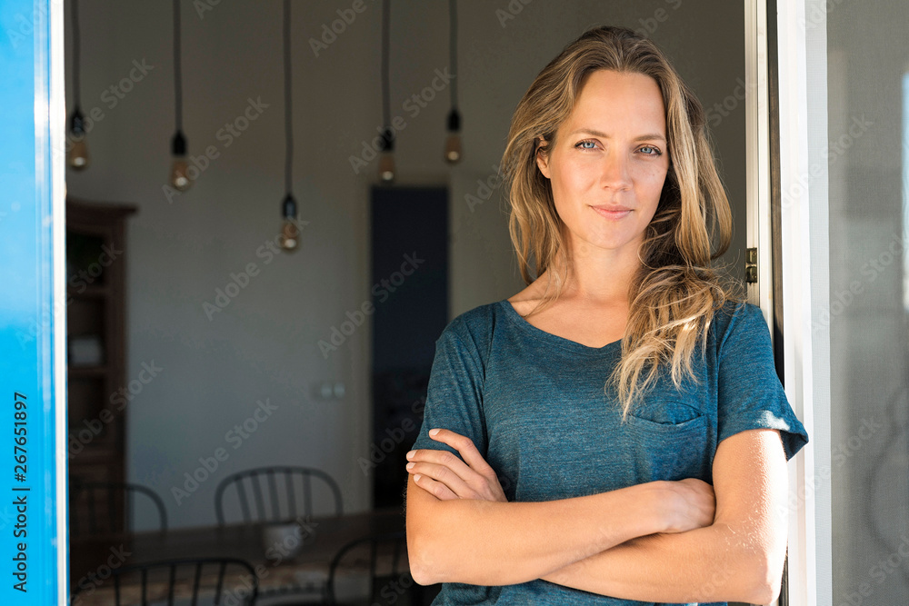 Portrait of confident woman leaning at open window at home