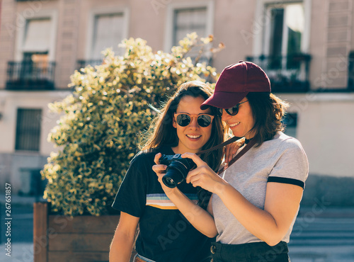 A couple of gay woman sightseeing together, smiling and looking his reflex photo camera. Same sex young married female couple showing some affection LGBT in Madrid.