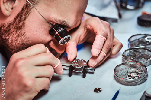 Expirienced clockmaster is fixing old watch for a customer at his repairing workshop. photo