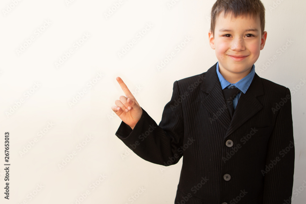 schoolboy boy in black business suit shows hand with smile on his face schoolboy boy in black business suit shows hand with smile on his face