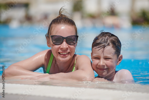 Smiling European woman and her son are having fun at the hotel’s swimming pool. They are at their summer vacations.