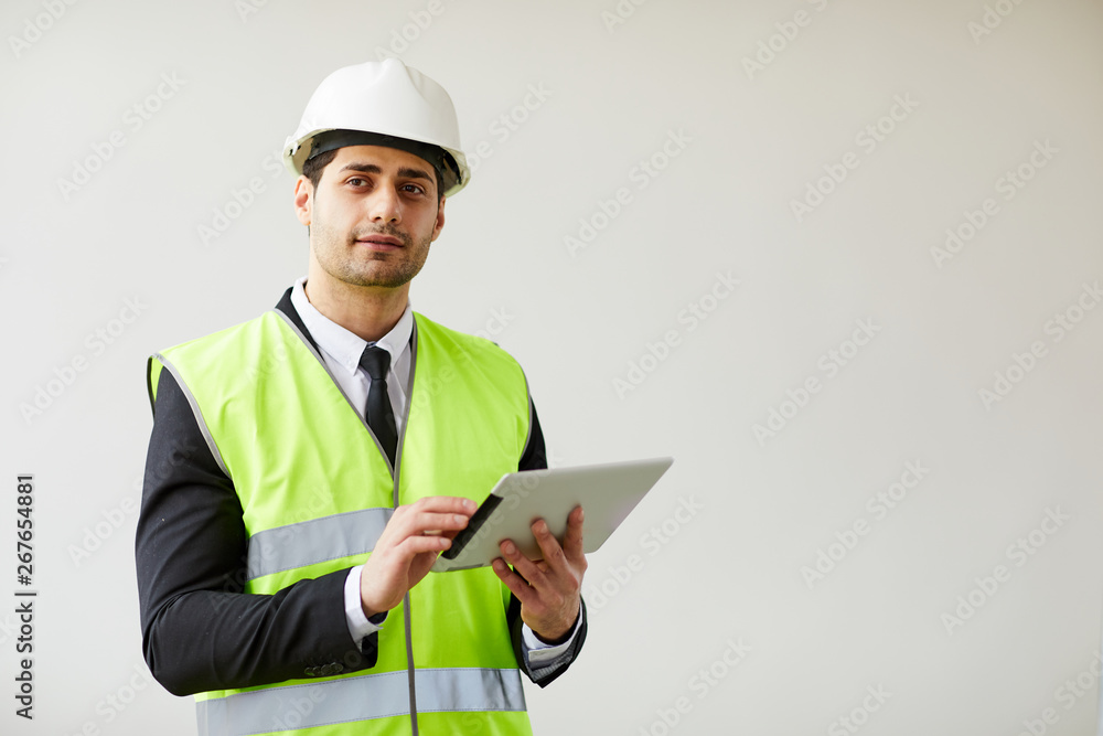 Waist up portrait of Middle-Eastern engineer wearing hardhat posing against white background holding tablet, copy space Waist up portrait of Middle-Eastern engineer wearing hardhat posing against white background holding tablet, copy space