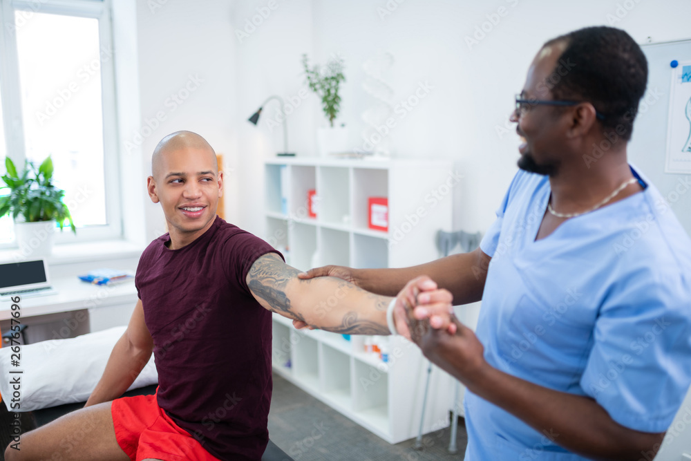 Fototapeta premium Dark-eyed sportsman with tattoo on arm visiting physical therapist