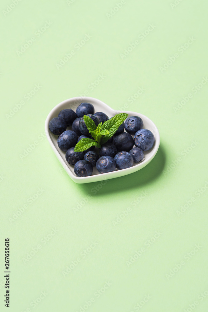 Fresh blueberries in heart shaped plate on pastel green background. Healthy breakfast concept Fresh blueberries in heart shaped plate on pastel green background. Healthy breakfast concept