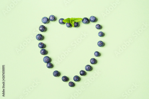 Fresh blueberries in shape of heart frame on pastel green background. Healthy breakfast concept
