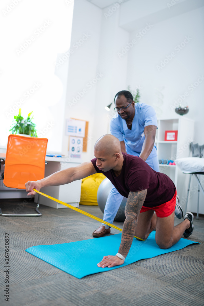 Sportsman doing exercises on sport mat while visiting therapist Sportsman doing exercises on sport mat while visiting therapist