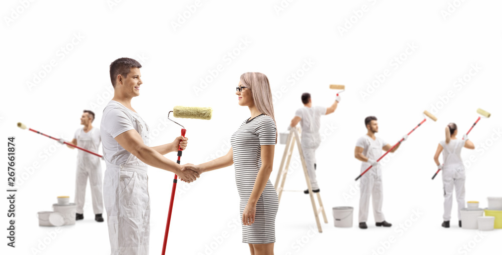 Male painter shaking hands with a young woman and workers painting wall
