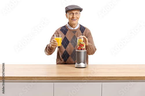 Cheerful elderly man preparing fruit in a blender and holding a glass of fresh juice