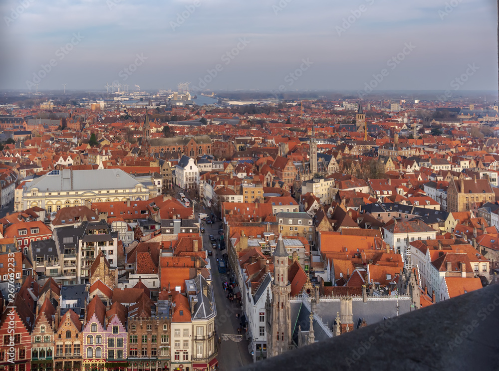 Fantastic Bruges city skyline with red tiled roofs and numerous churches' towers in sunny winter day. View to Bruges medieval cityscape from the top of the Belfry Tower.