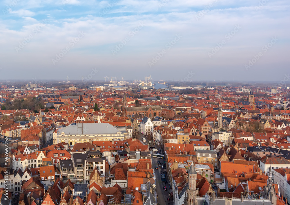 Fantastic Bruges city skyline with red tiled roofs and numerous churches' towers in sunny winter day. View to Bruges medieval cityscape from the top of the Belfry Tower.