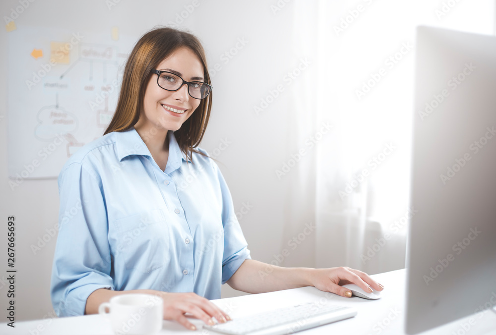 Smiling young female manager working at the computer. Happy business woman sitting on the workplace in the office. Smiling young female manager working at the computer. Happy business woman sitting on the workplace in the office.
