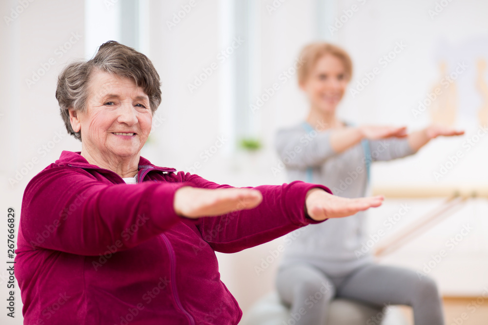Smiling elderly lady holding her arms during pilates for seniors Smiling elderly lady holding her arms during pilates for seniors