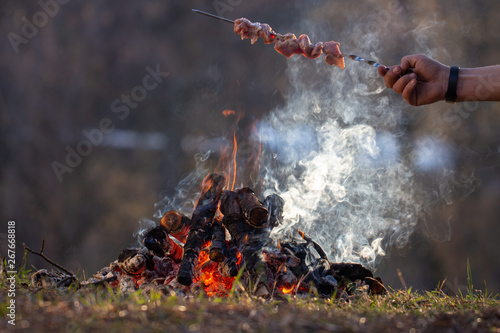 Fresh meat skewers on a metal skewer in a man's hand over ongnym in the forest