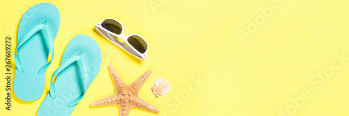 Blue flip flops, swimsuit, sunglasses and starfish on yellow background.