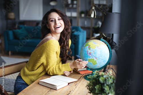 Smiling woman with a model of the globe selects a country for travel.