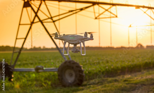Drone flying in front of irrigation system in field at sunset