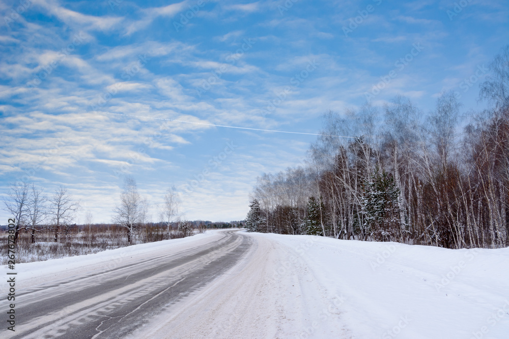 Patterns on the winter highway in the form of four straight lines. Snowy road on the background of snow-covered forest. Winter landscape. Patterns on the winter highway in the form of four straight lines. Snowy road on the background of snow-covered forest. Winter landscape.