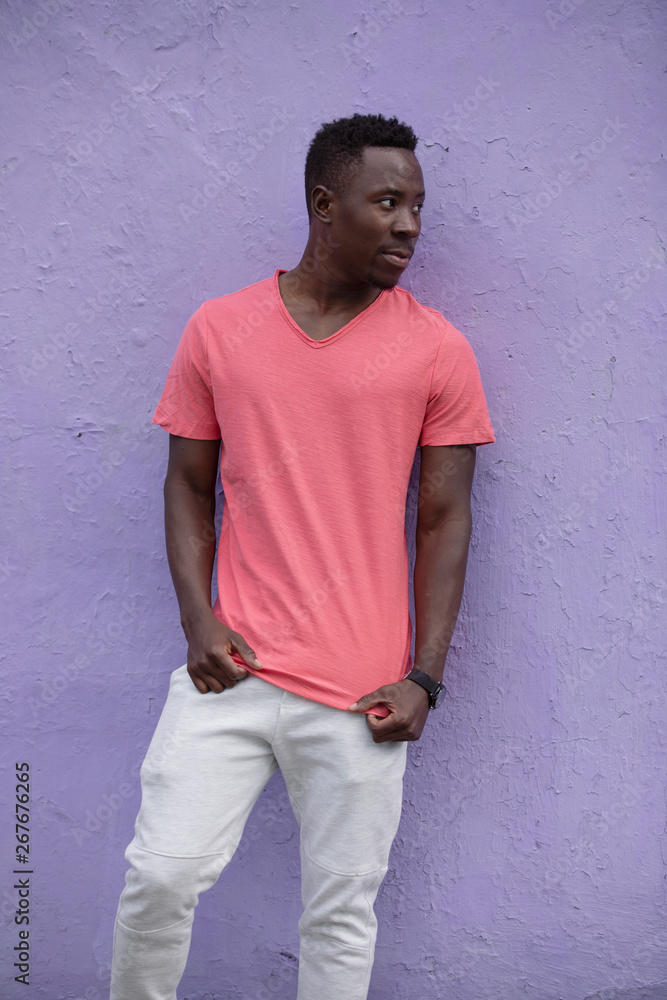 African American man model posing in empty living coral color t-shirt standing against violet wall background African American man model posing in empty living coral color t-shirt standing against violet wall background