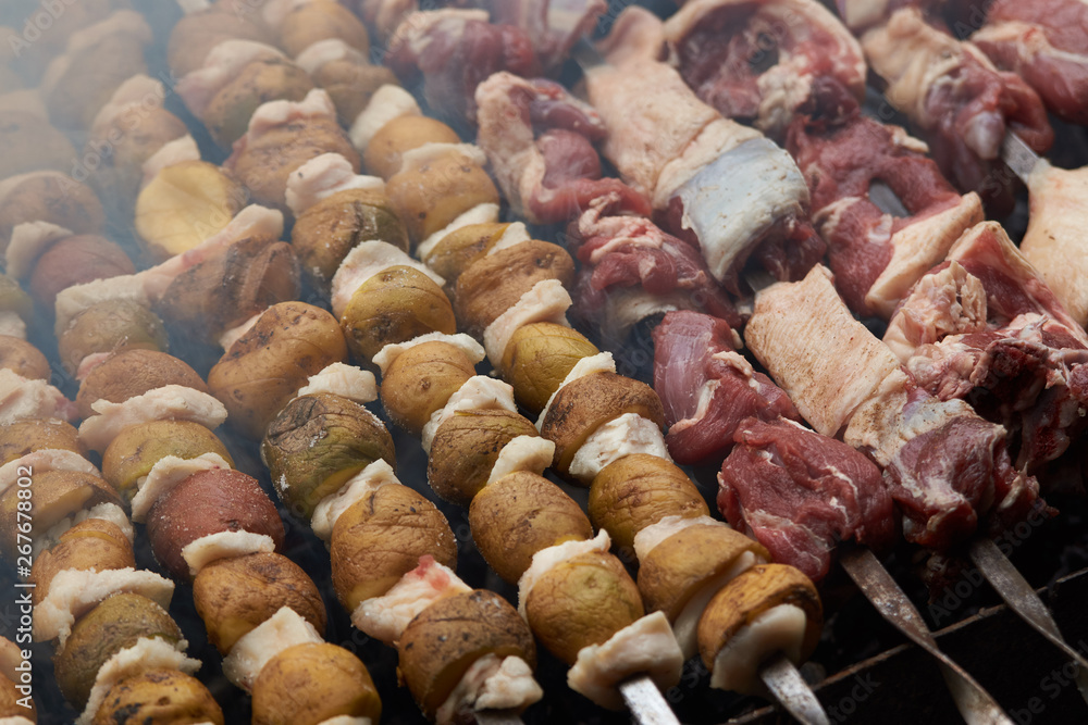Preparation of shish kebab on skewers, close-up. BBQ grill with lamb meat and potatoes Preparation of shish kebab on skewers, close-up. BBQ grill with lamb meat and potatoes