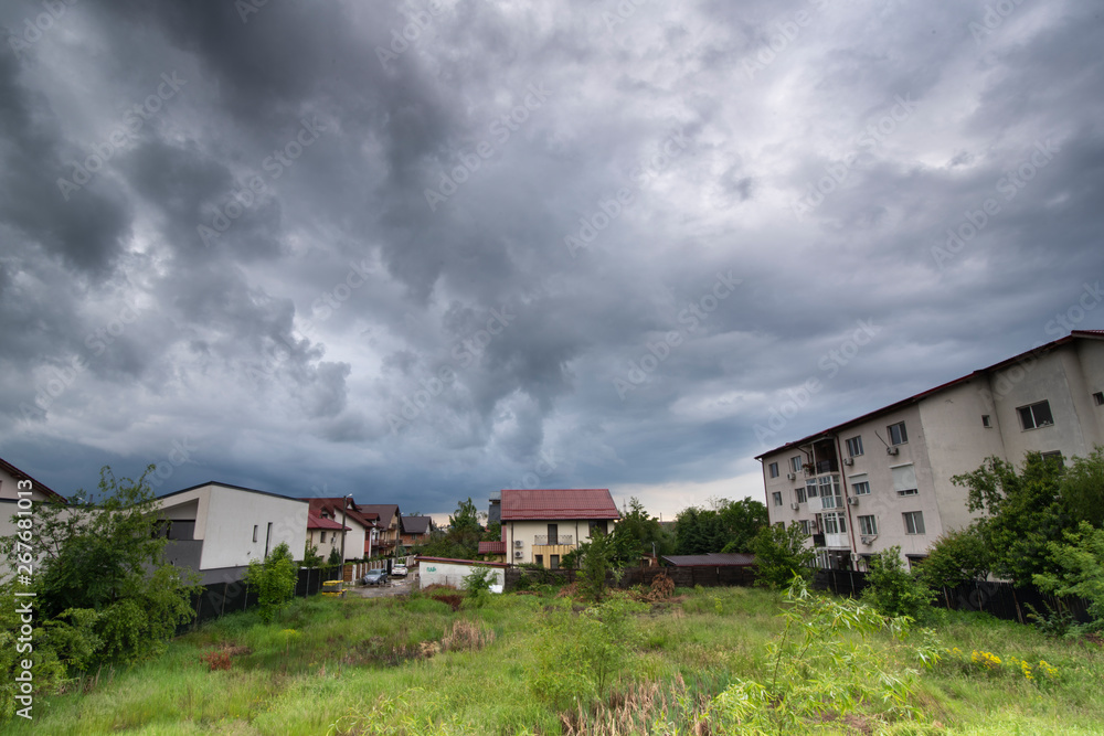 Green grass and houses under dark sky with clouds before storm Green grass and houses under dark sky with clouds before storm