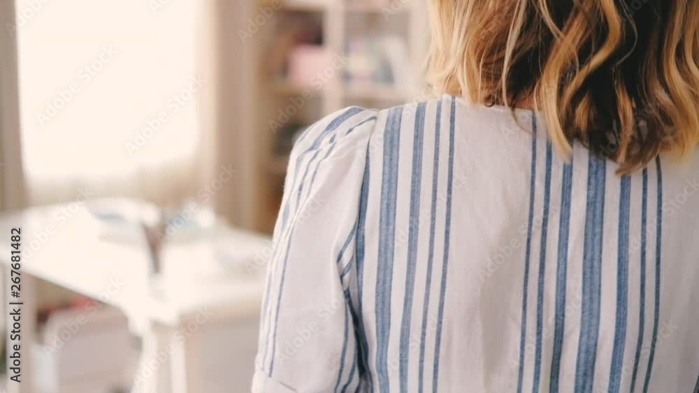 Home art studio atmosphere. Female going across workroom. Delicate hand touching desk with sketchbooks supplies on. Home art studio atmosphere. Female going across workroom. Delicate hand touching desk with sketchbooks supplies on.
