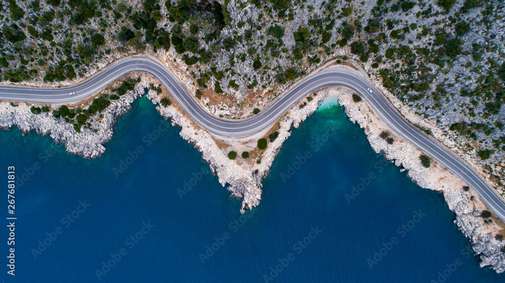 Obraz premium Aerial landscape of coastline and a road seascape. Car drives down the empty asphalt road running along the sunny Mediterranean shoreline of Turkey. Tourist car cruises down the scenic coastal road .