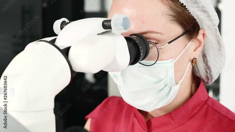 Close-up A woman in glasses with a professional dentist working with a professional stamotological microscope in her office. Stamotologist profession concept Close-up A woman in glasses with a professional dentist working with a professional stamotological microscope in her office. Stamotologist profession concept