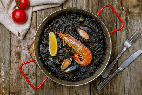 black paella with seafood on wooden background photo