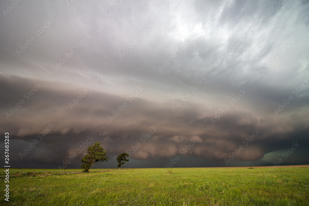 A dark supercell storm with a low shelf cloud fills the sky over a ...