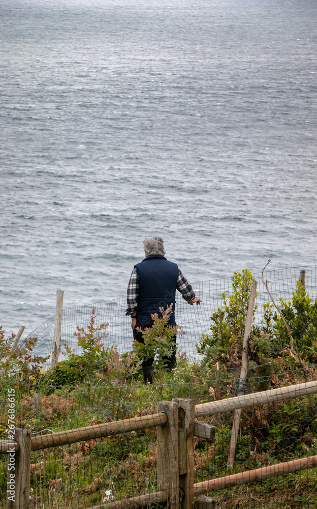 Elderly man from behind watching the sea on an Atlantic cliff in Galicia, Spain.