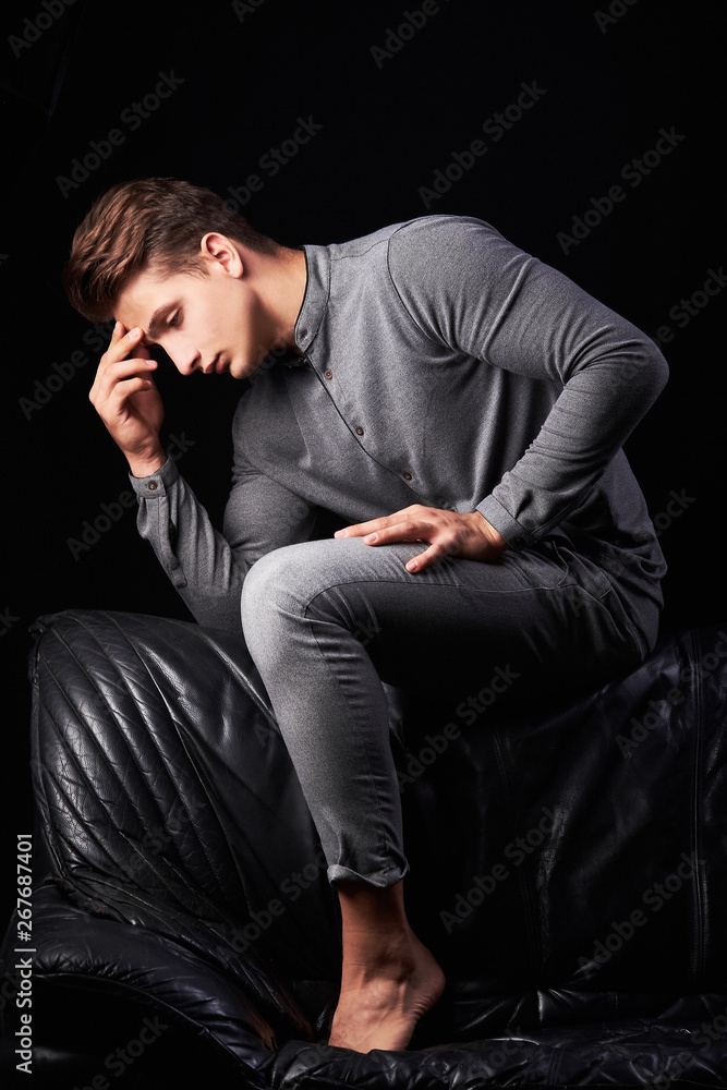 Fashion portrait of elegant young man sitting on leather sofa on black background Fashion portrait of elegant young man sitting on leather sofa on black background