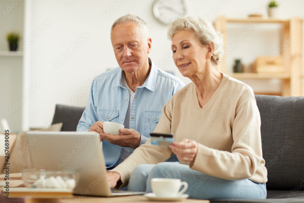 Warm toned portrait of modern senior couple shopping online or paying taxes holding credit card while using laptop at home, copy space Warm toned portrait of modern senior couple shopping online or paying taxes holding credit card while using laptop at home, copy space